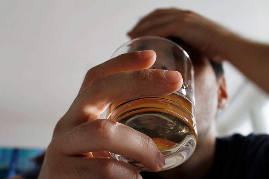 Tight shot of a man's hand holding a glass of brown liquor.
